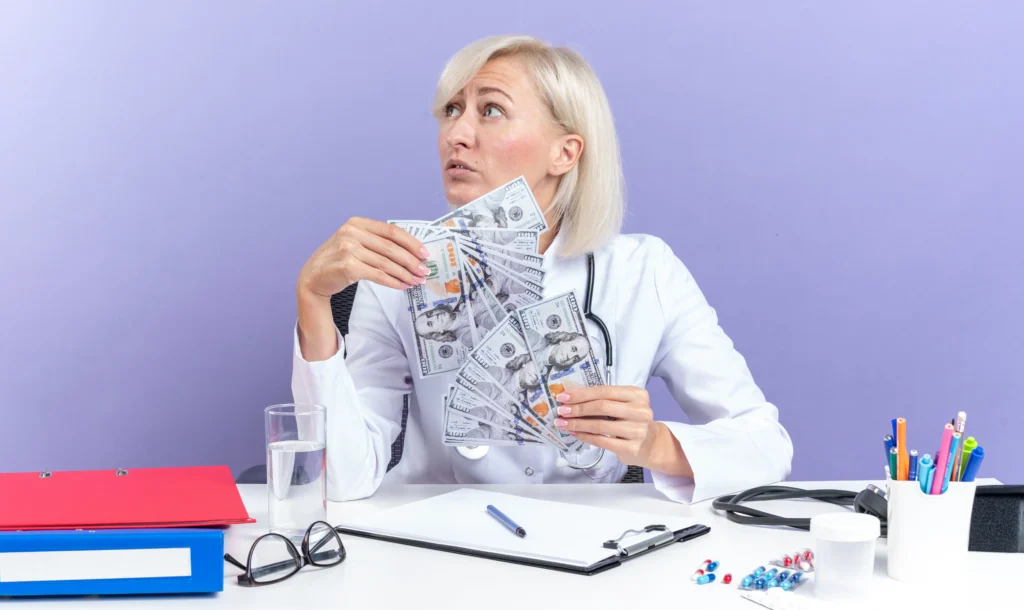 Une femme en blouse blanche tient des billets et réfléchit, au bureau.