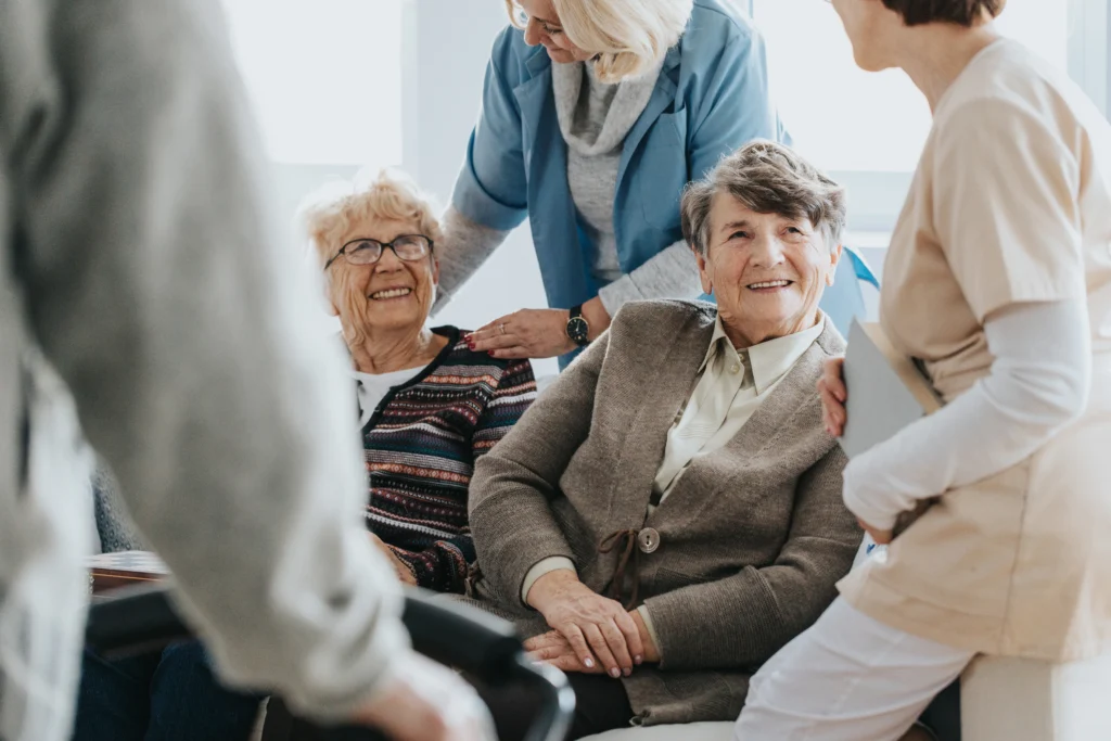 Deux personnes âgées assises sur un canapé, accompagnées par un soignant.