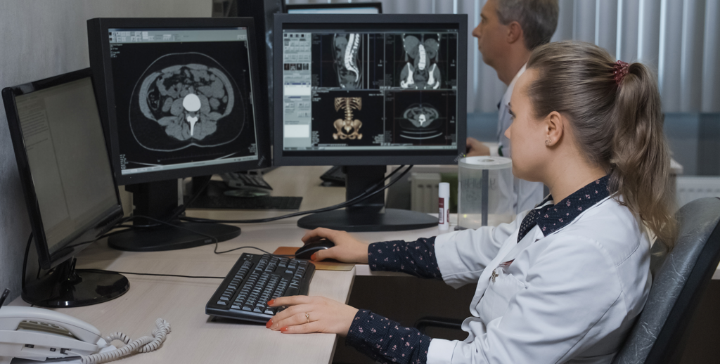 Deux professionnels analysent des images médicales sur des écrans en salle de radiologie.